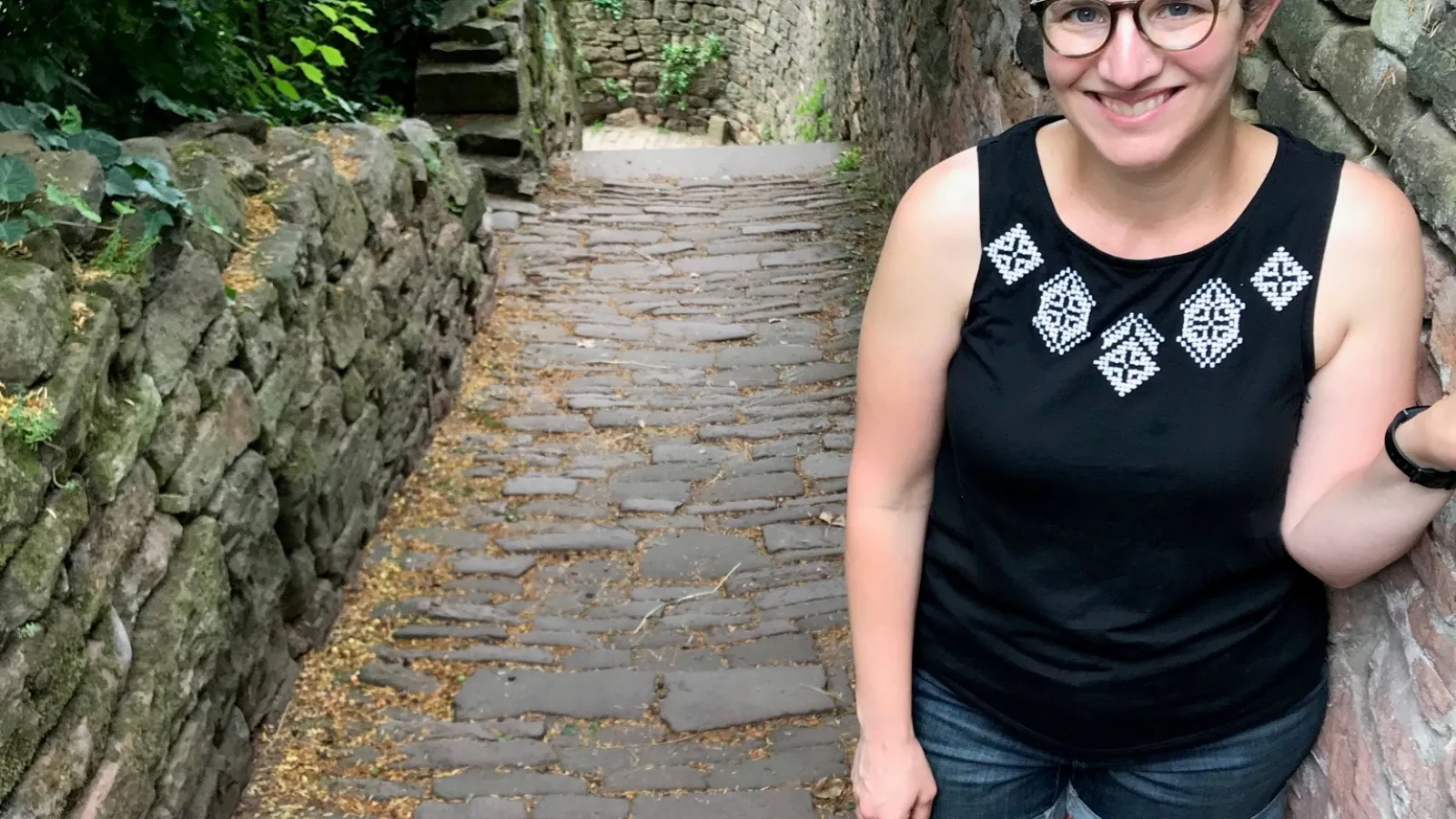 TPS Fellow Katie D'Amico-Willman standing next to a stone wall in an outdoor forested area