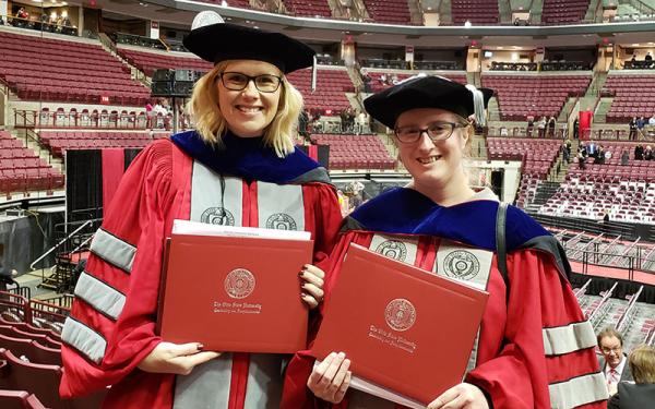 Two doctoral graduates holding diplomas