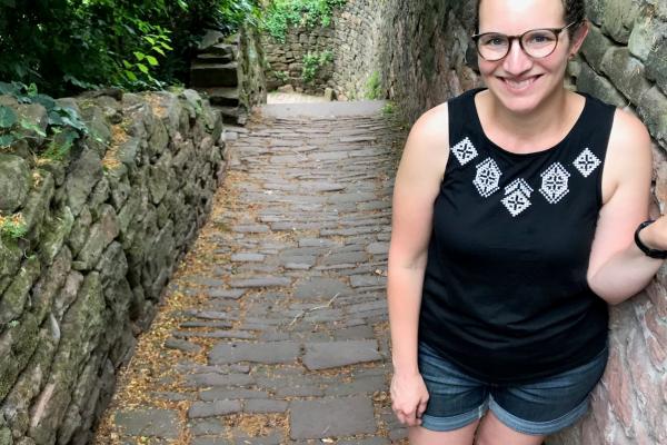 TPS Fellow Katie D'Amico-Willman standing next to a stone wall in an outdoor forested area